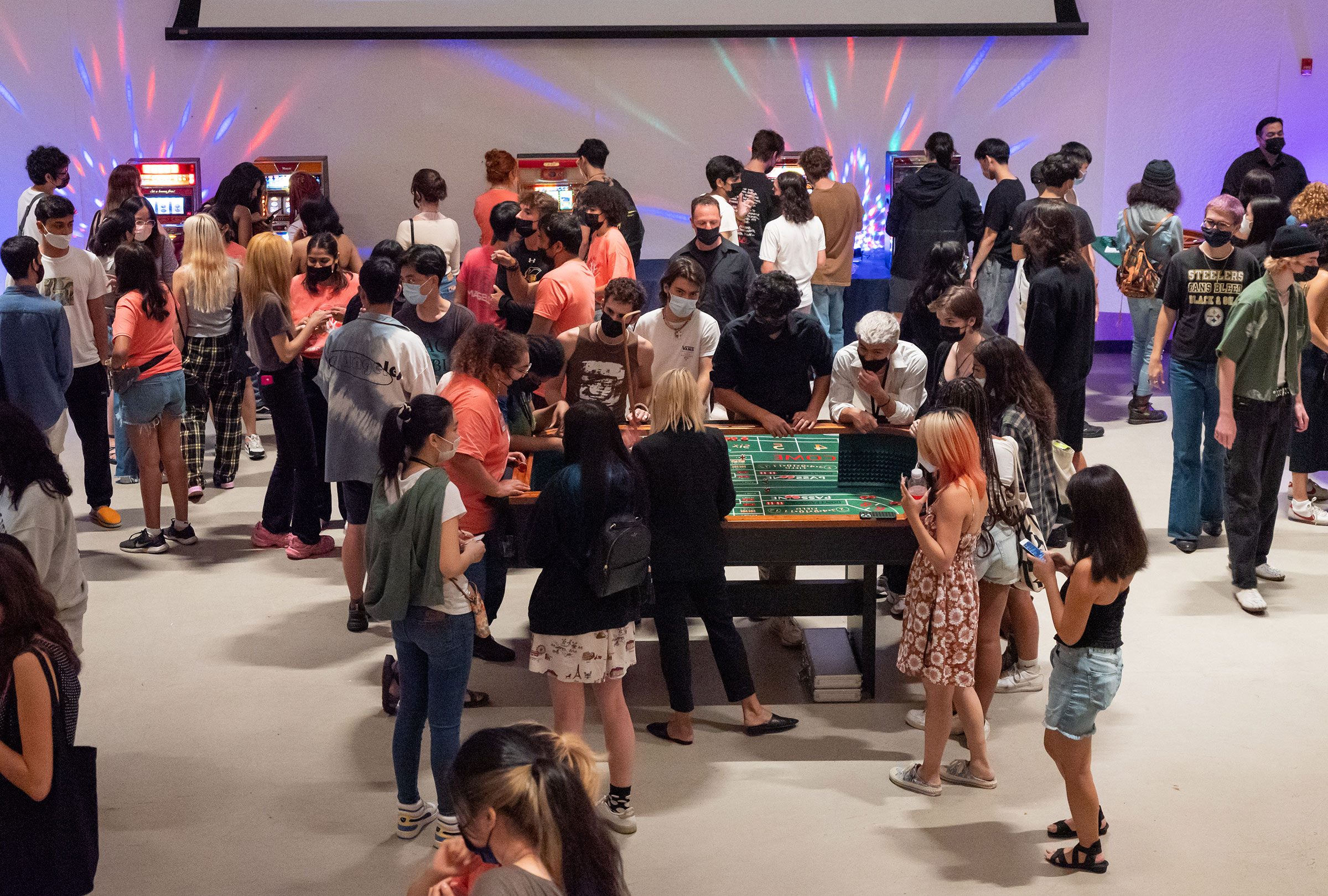 A crowd of students in the student union around different card tables and slot machines.