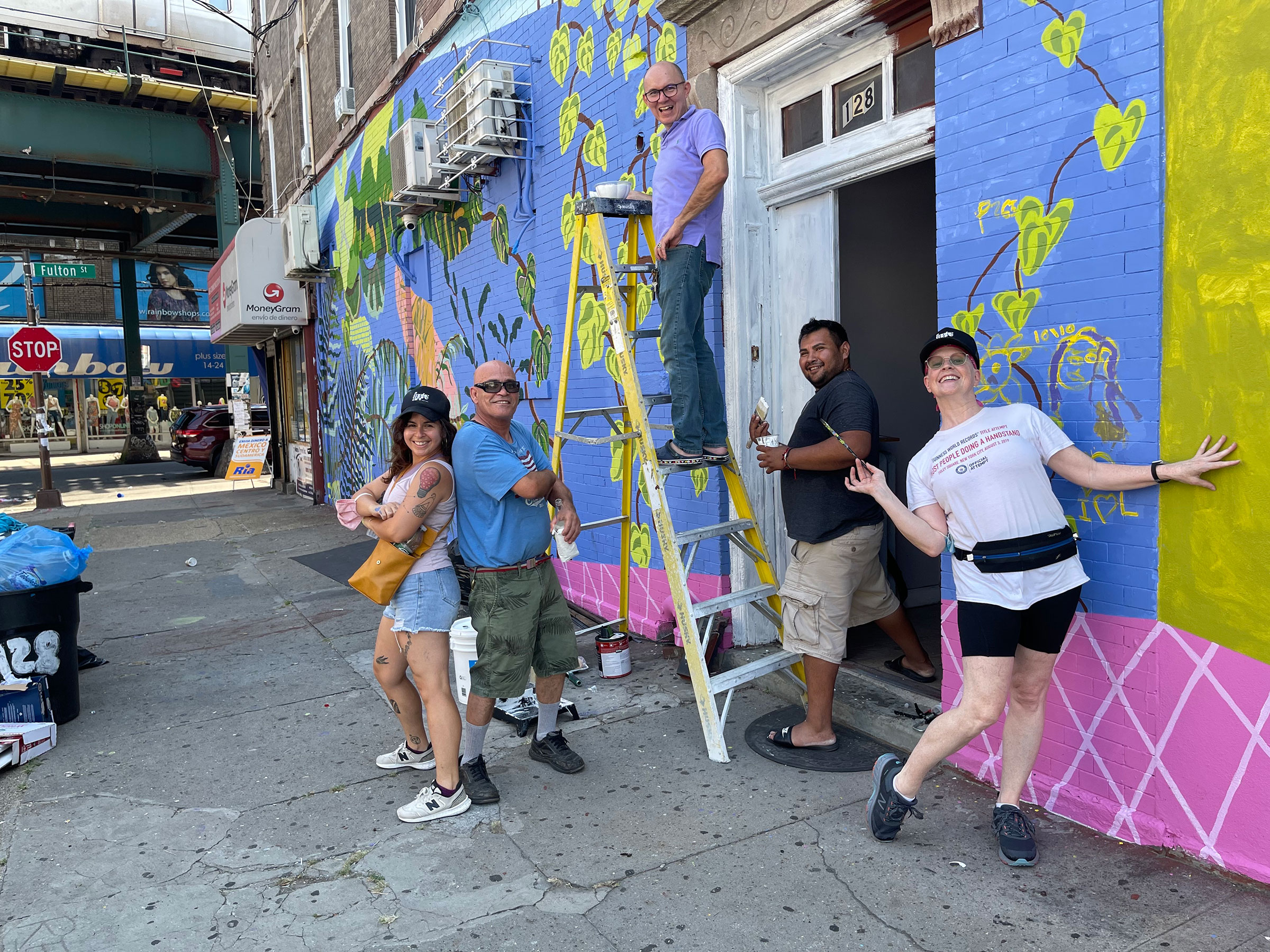 A group of people paint a mural on street close to subway tracks.