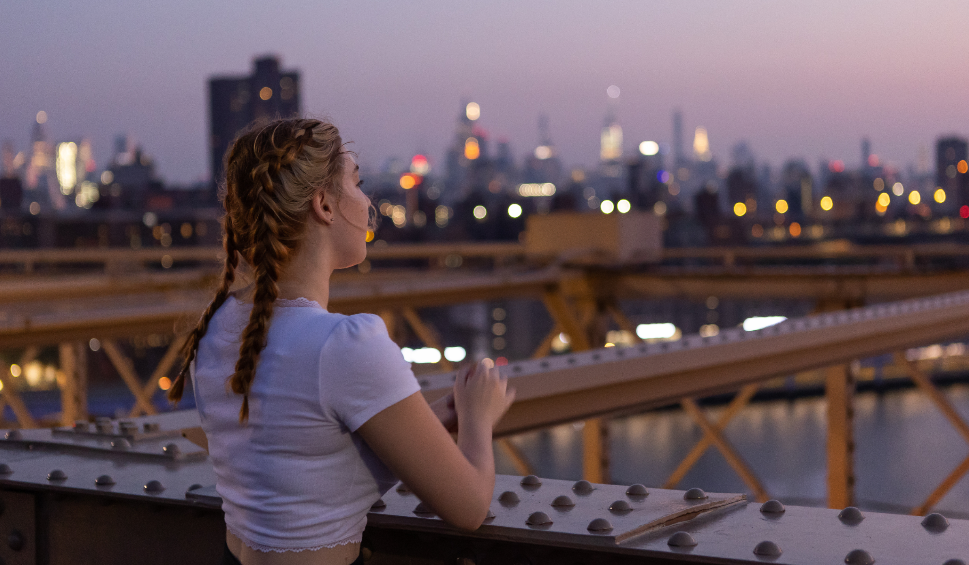 woman standing at brooklyn bridge, looking at brooklyn skyline and river