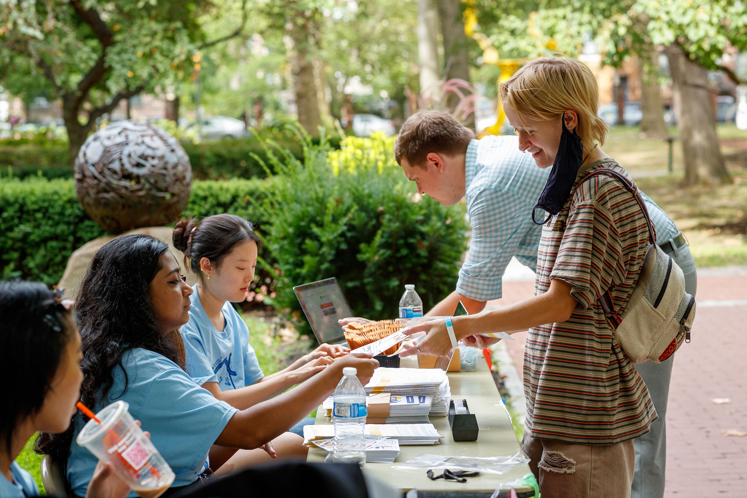 Two students are greeted by orientation staff at a long table on campus.
