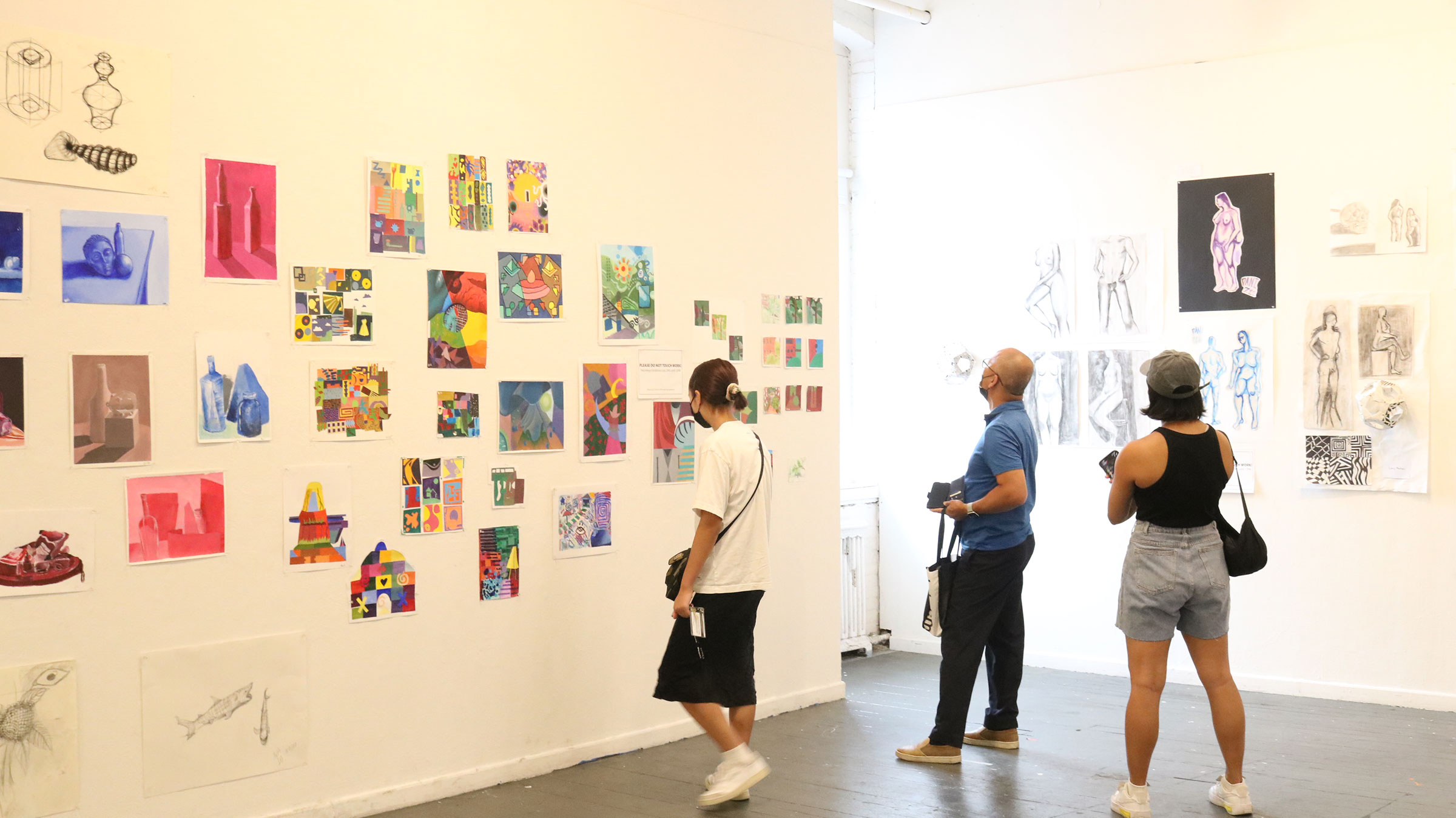 A group of people look at art displayed in a gallery.
