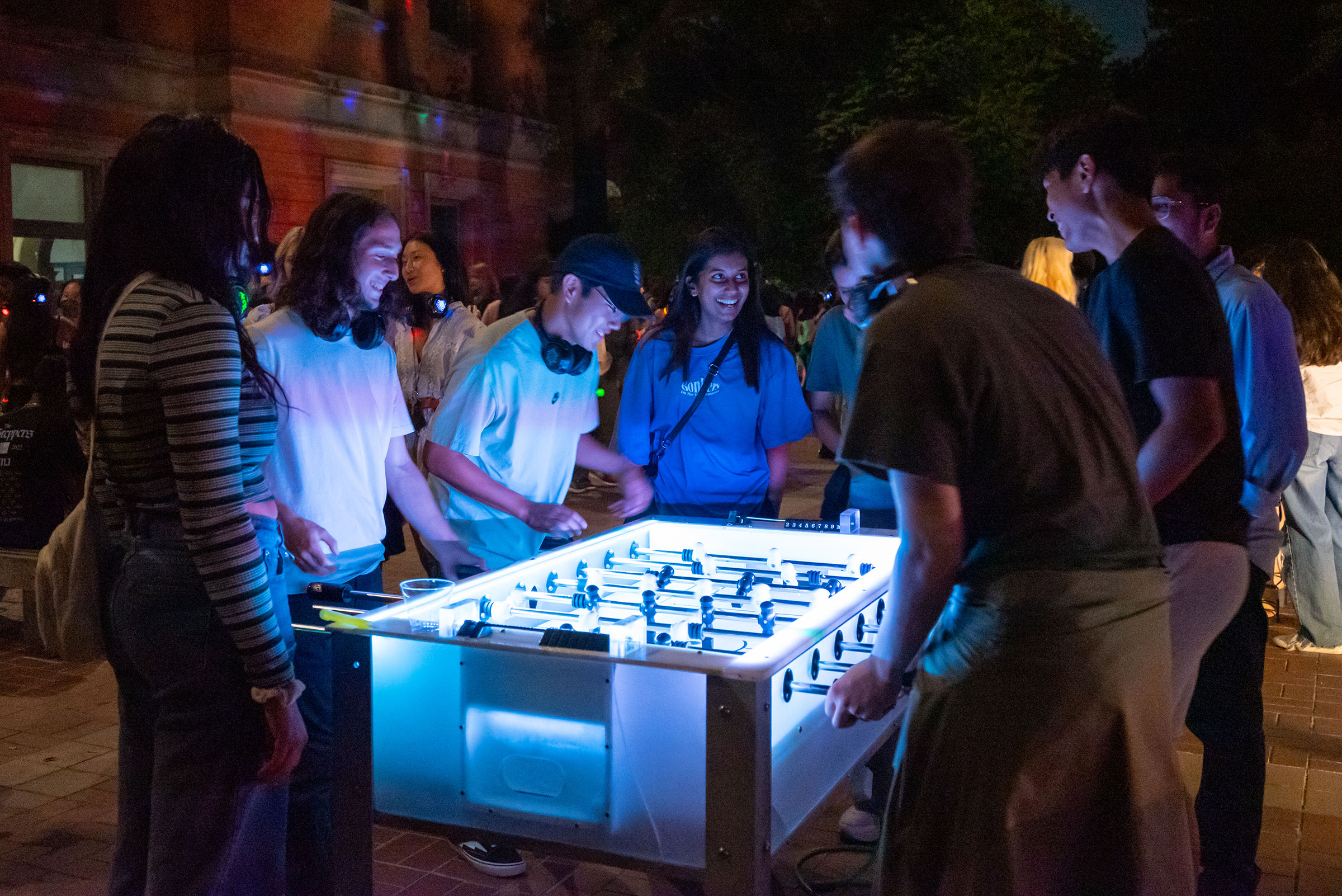 students standing around a glowing foosball table smiling and playing.