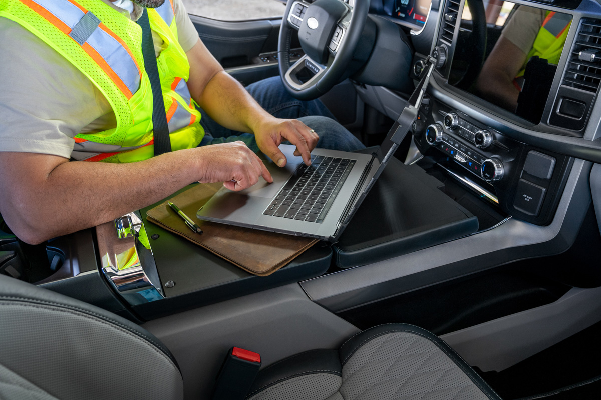 Auto console with hidden transmission shifter transformed into work surface for person in driver’s seat typing on laptop