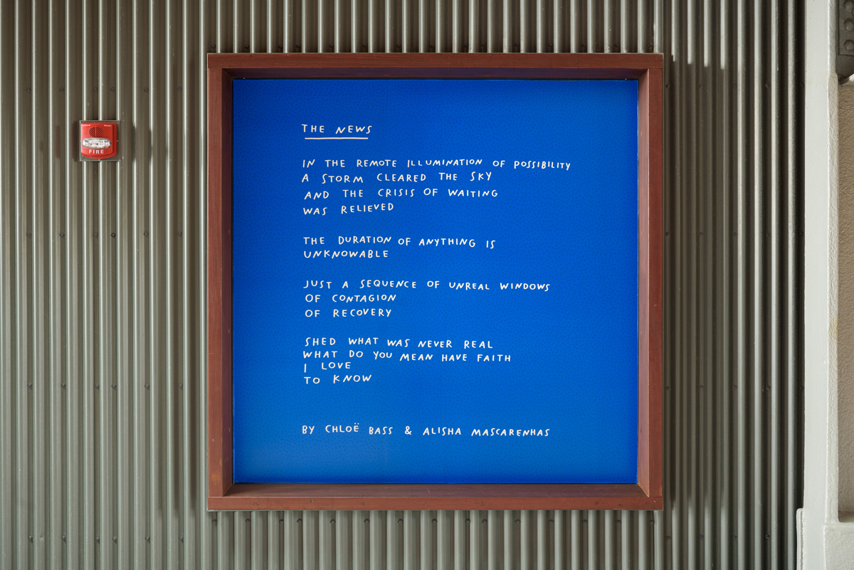 Installation of poem titled “The News,” printed in white on bright blue background, framed on a corrugated wall