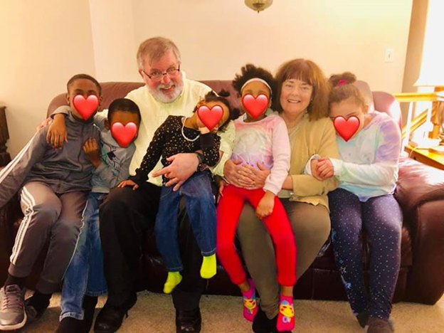 Five children nestled on a couch with foster parents Michael and Nancy Borghese, with hearts on the children’s faces for privacy