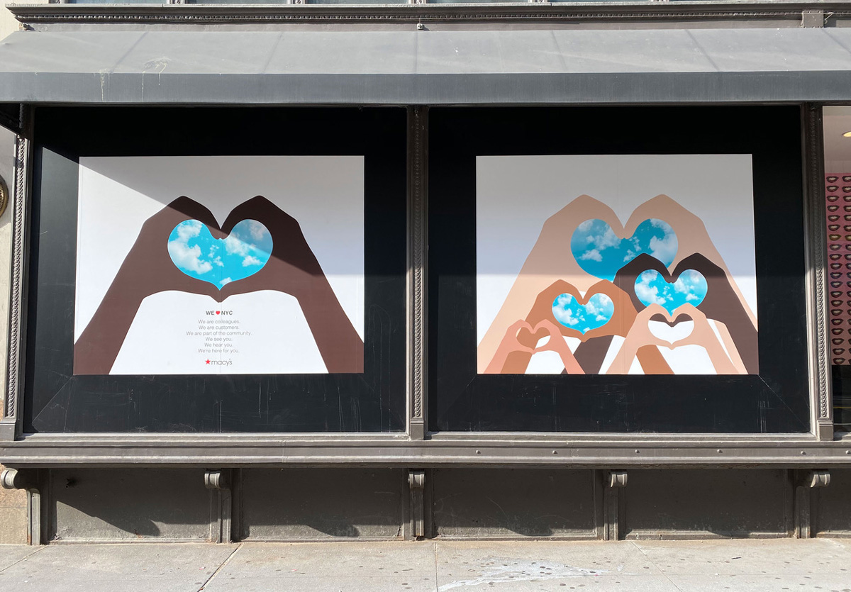 Department store windows featuring illustrated hands of different skin tones forming heart shapes around blue sky with clouds