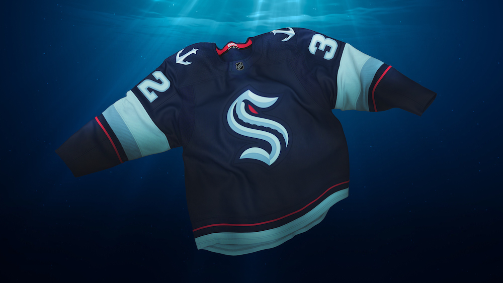 A dark-blue hockey jersey with a large S in gothic typeface on its front and white anchors on its shoulders floats underwater with thin beams of light from the surface