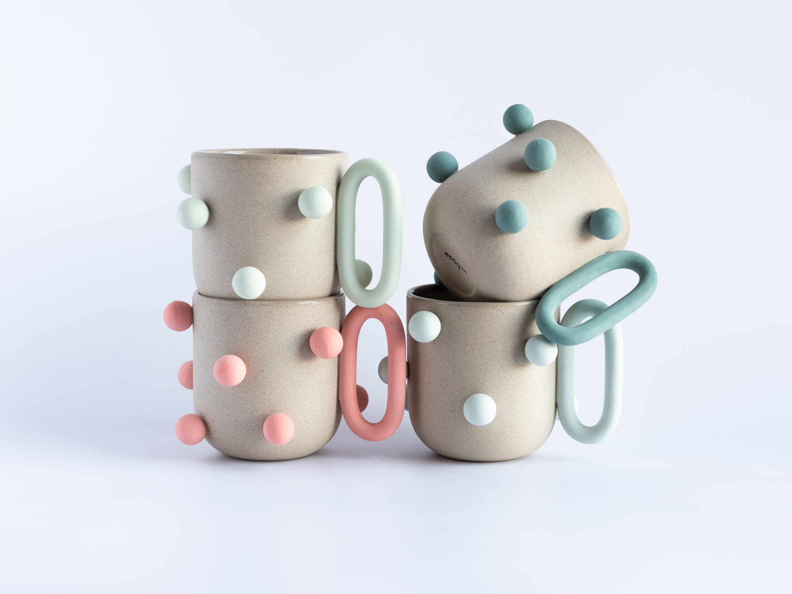 Four ceramic mugs with large oval handles and colorful spheres affixed to the sides