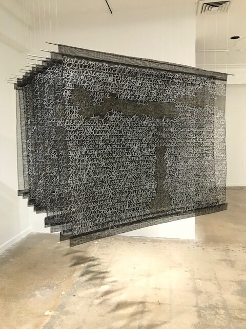 Translucent black squares with white inscription suspended from a gallery ceiling