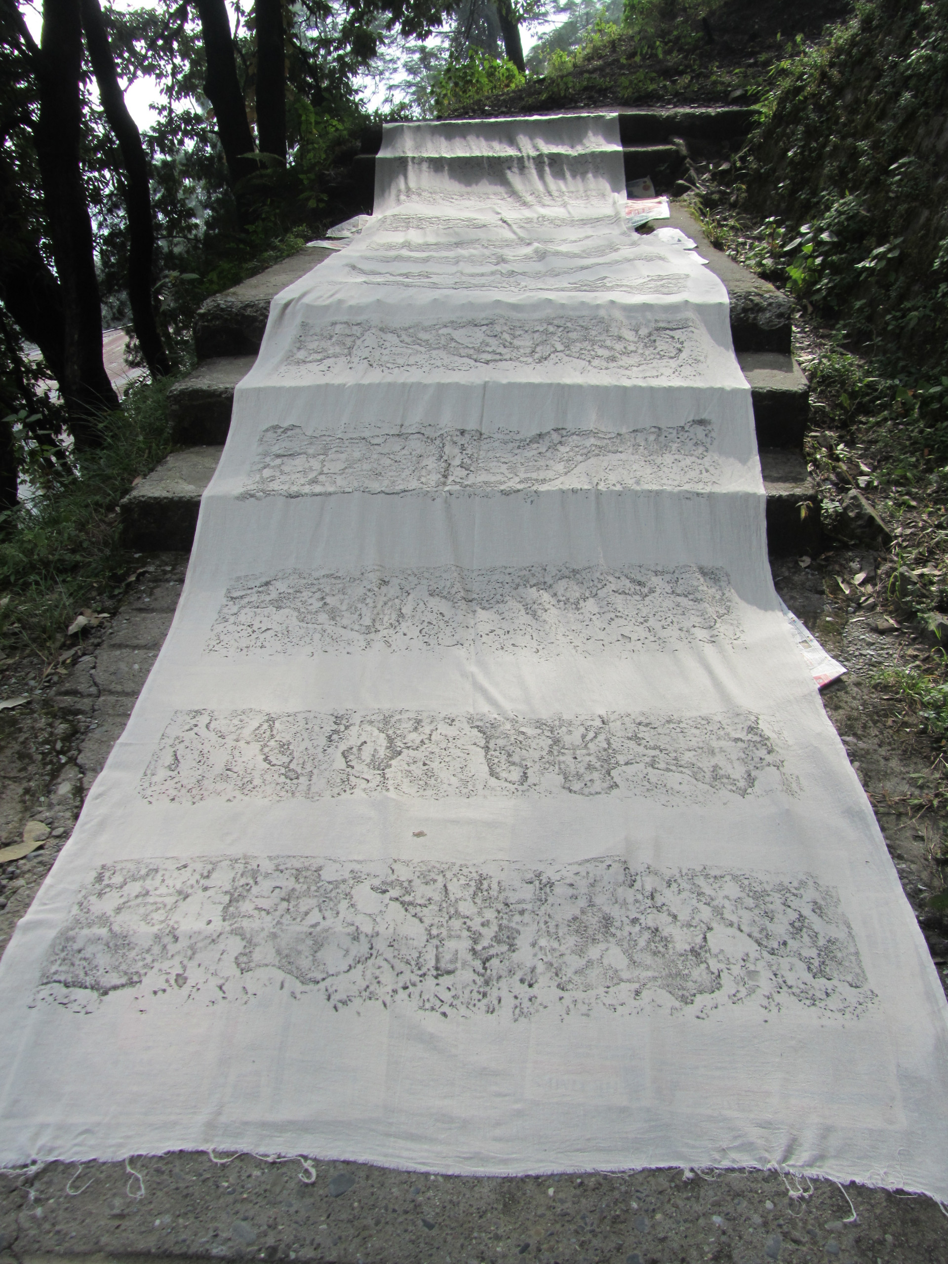 A long swath of white fabric lays on a footpath with steps, and gray markings on the fabric describe the ground surface beneath