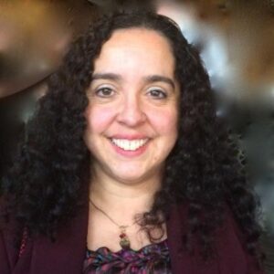 Esmilda Abreu smiles directly at the camera. The background is blurred.