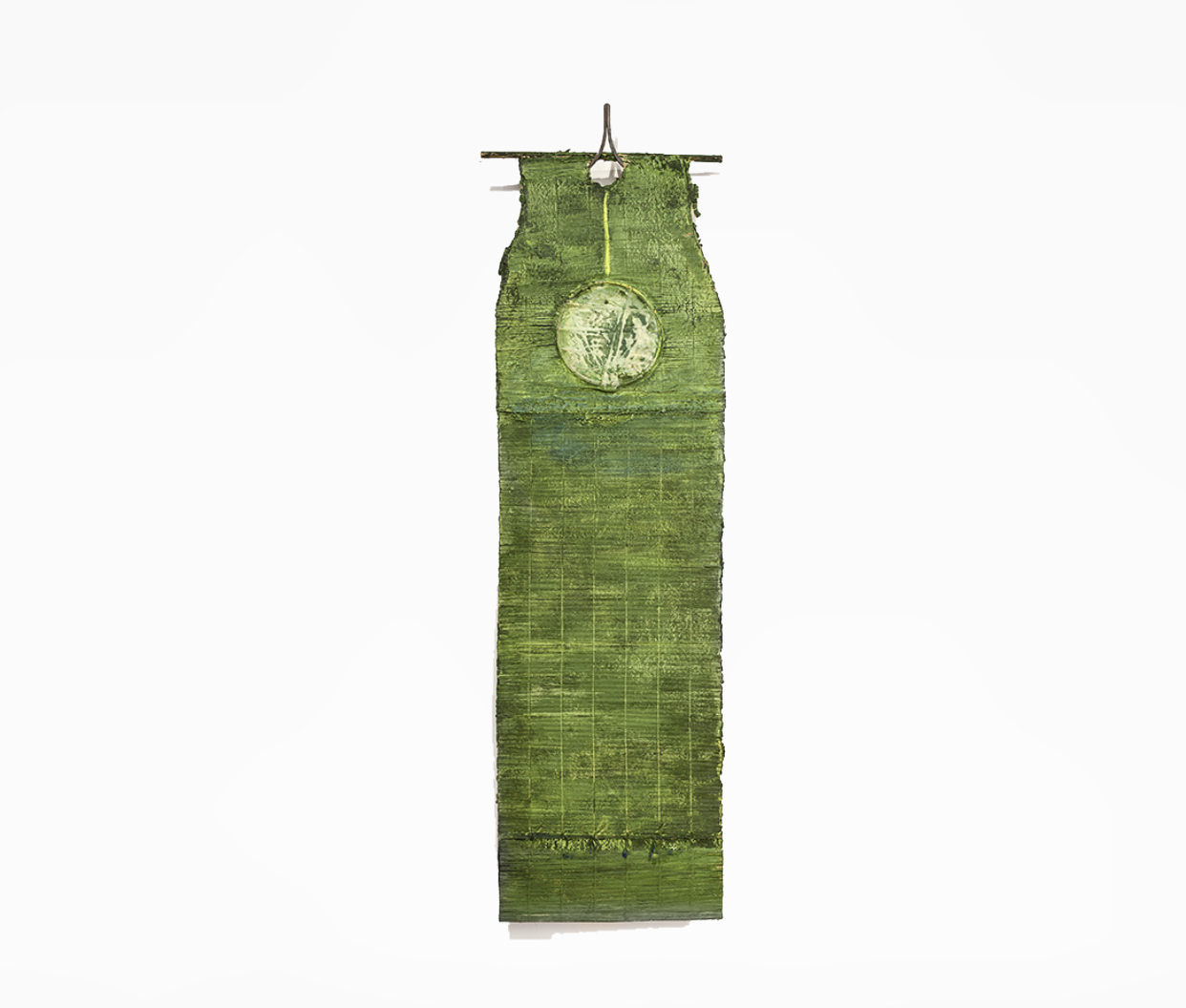 A flat, hanging sculpture made of woven paper colored green with a white circle near the top, hung from a thin brown rod
