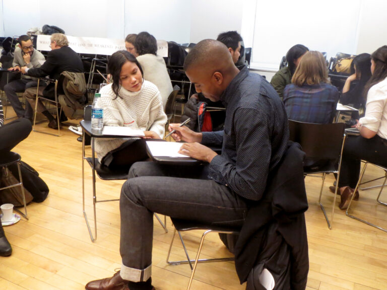 classroom of students, seated in desks, working in groups of two