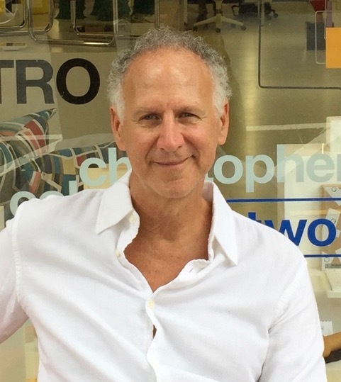 headshot of Gary Hattem, wearing white shirt, in front of glass window with words and text