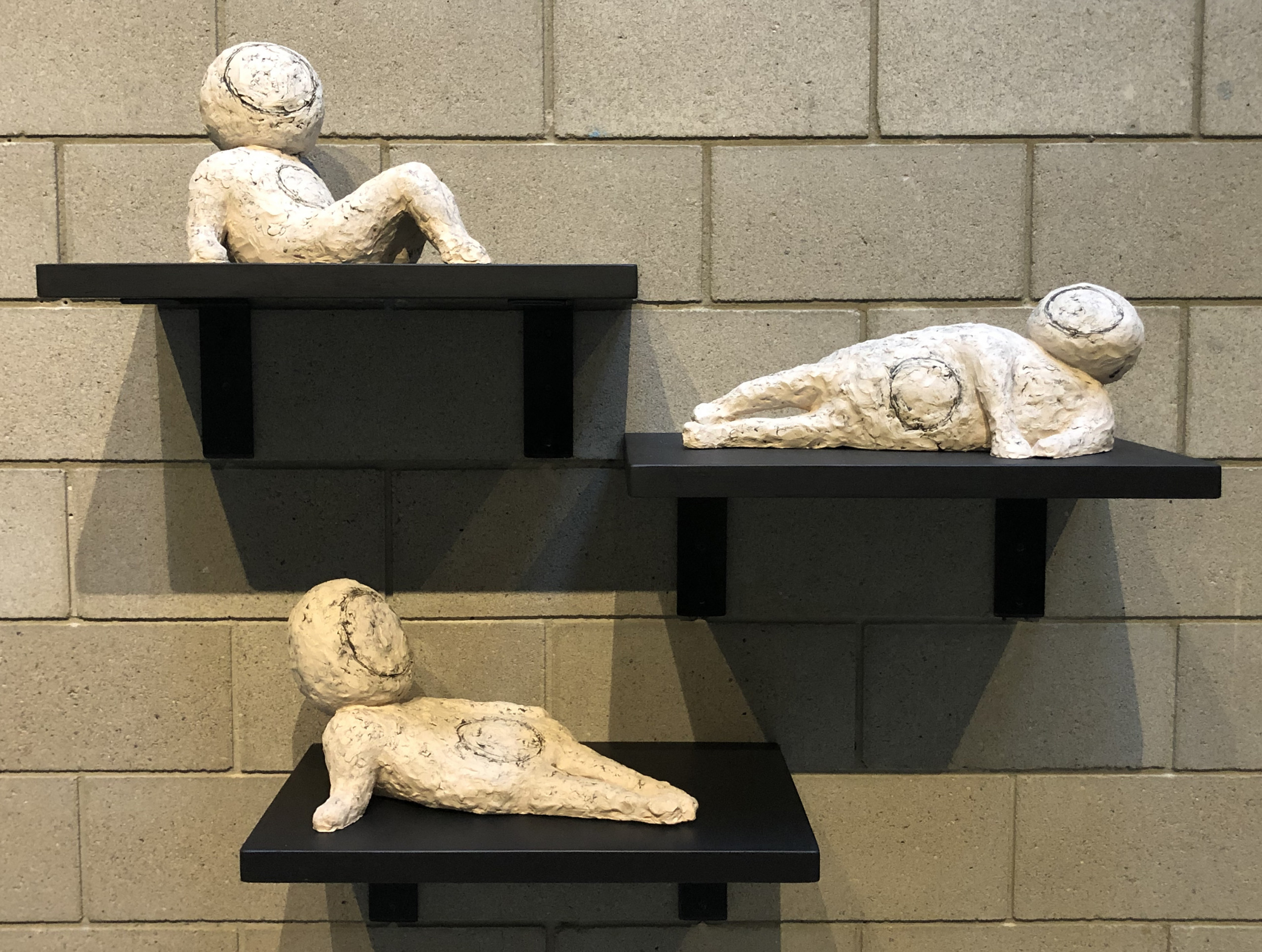 Three small abstract sculptures of human figures in reclining poses