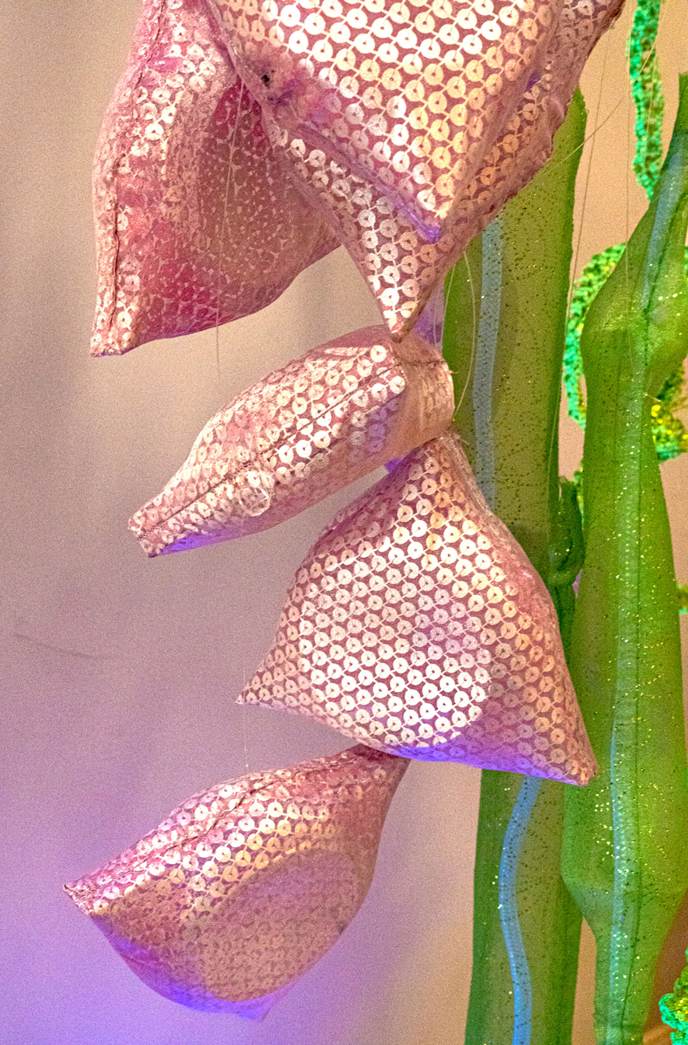 Triangular pink sequinned pouches cascade down cylindrical tubes made of green glittering organza