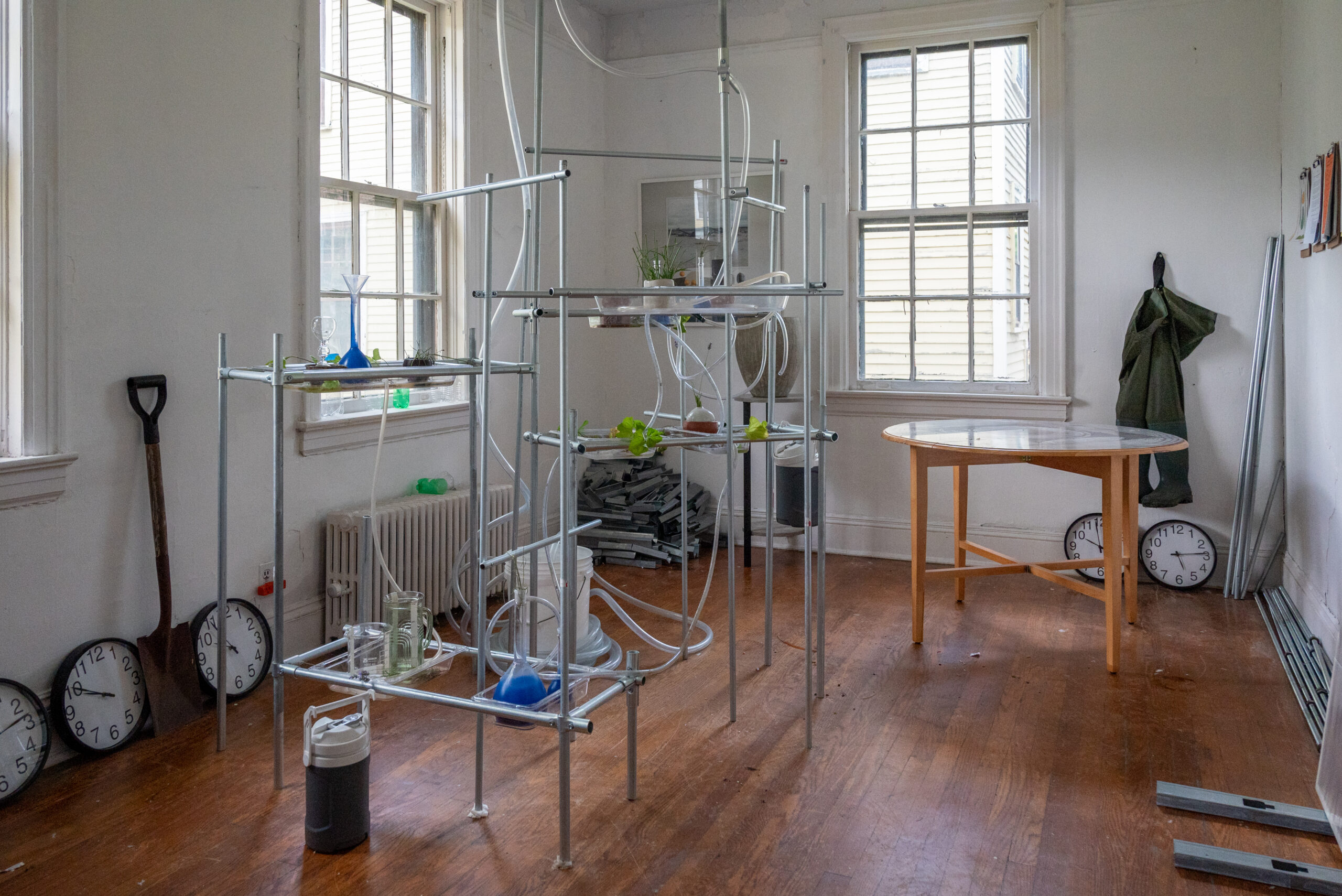 A metal framework holds tubes and vessels and several black and white clocks line the floor of a small room
