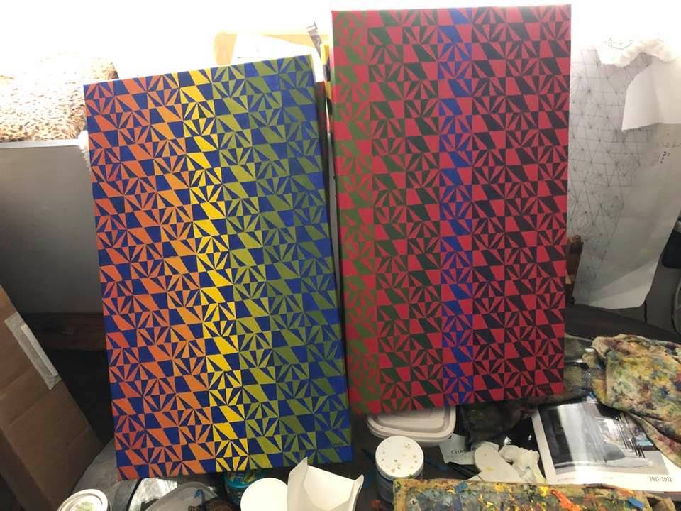 Two rectangular canvases painted with a checkered square-and-triangle pattern and gradient background color that shifts from red to yellow to blue and green to black