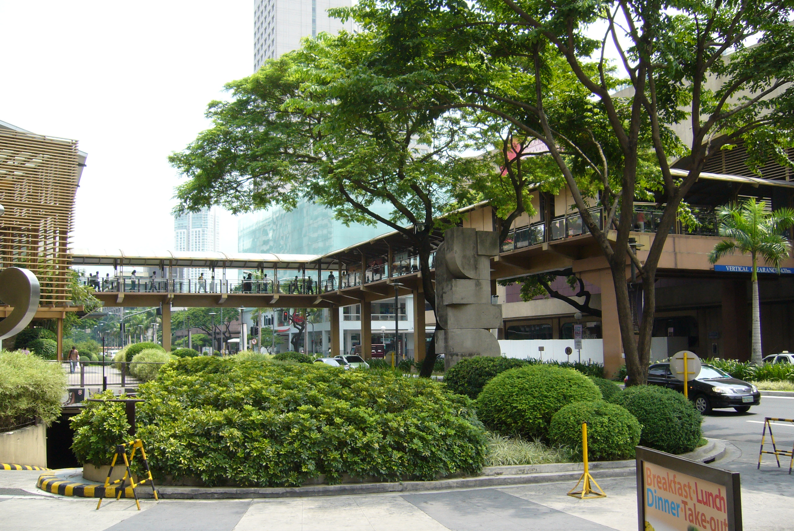 A a covered, open-air walkway with glass sides extends between two buildings and over a street