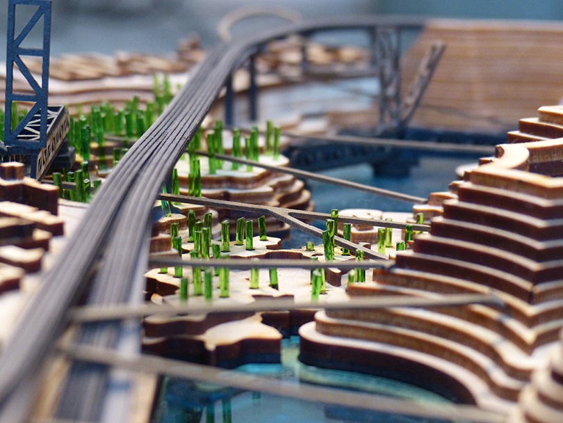 Miniature model of a bridge and rail system placed on a rocky, mountainous landscape.