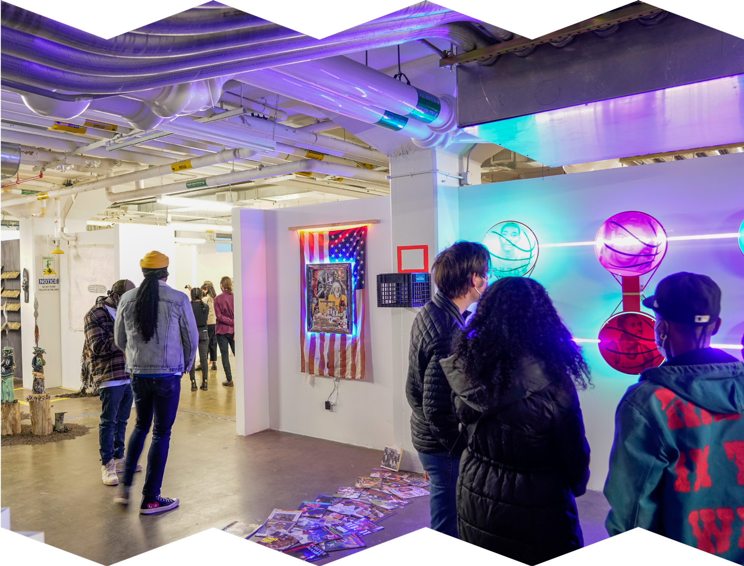 A photograph showing group exhibition of artwork: prints, sculptures, and neon lights. The space is full of people viewing and admiring the work.