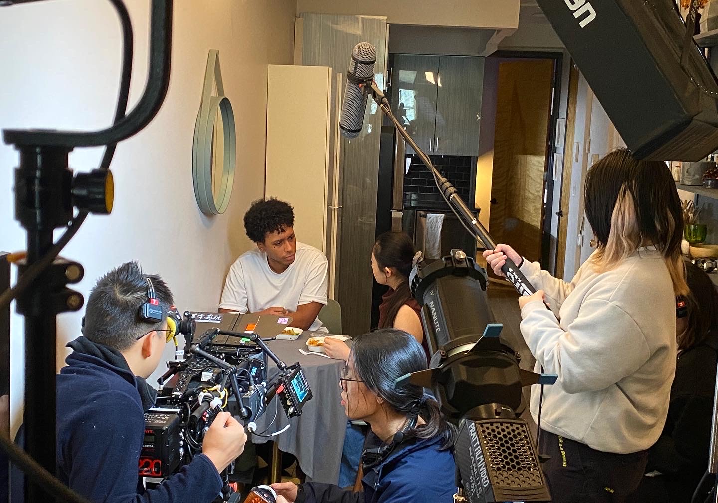 a photo of students making a film. a student holds a boom mic over head