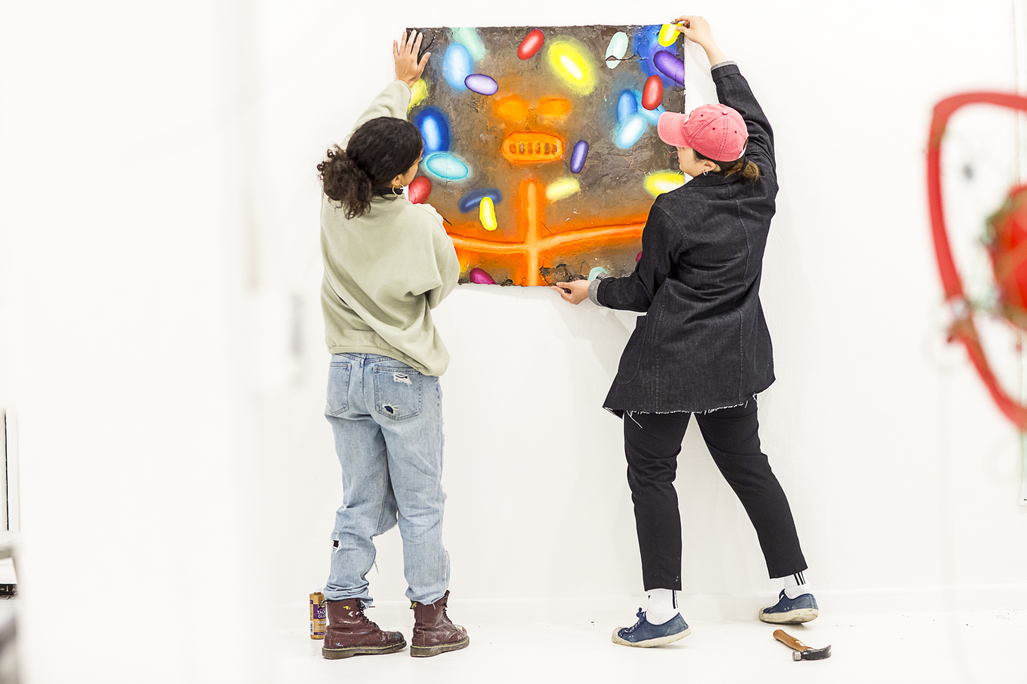 two students, hanging artwork together, in a large white gallery