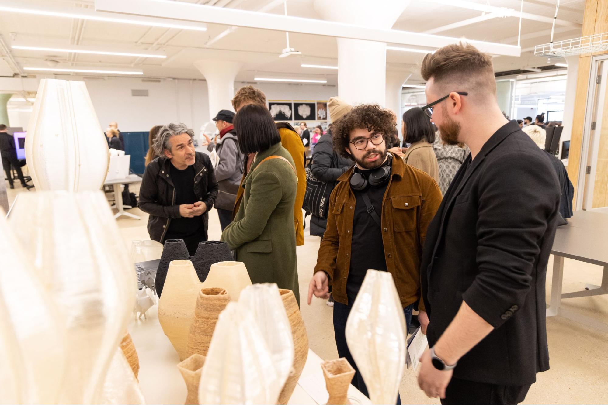 two people, in gallery room, discussing in front of oval vase sculptures in various materials