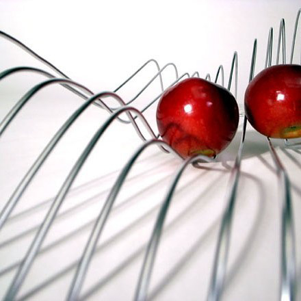 a fruit bowl made of wavy wires with two red apples