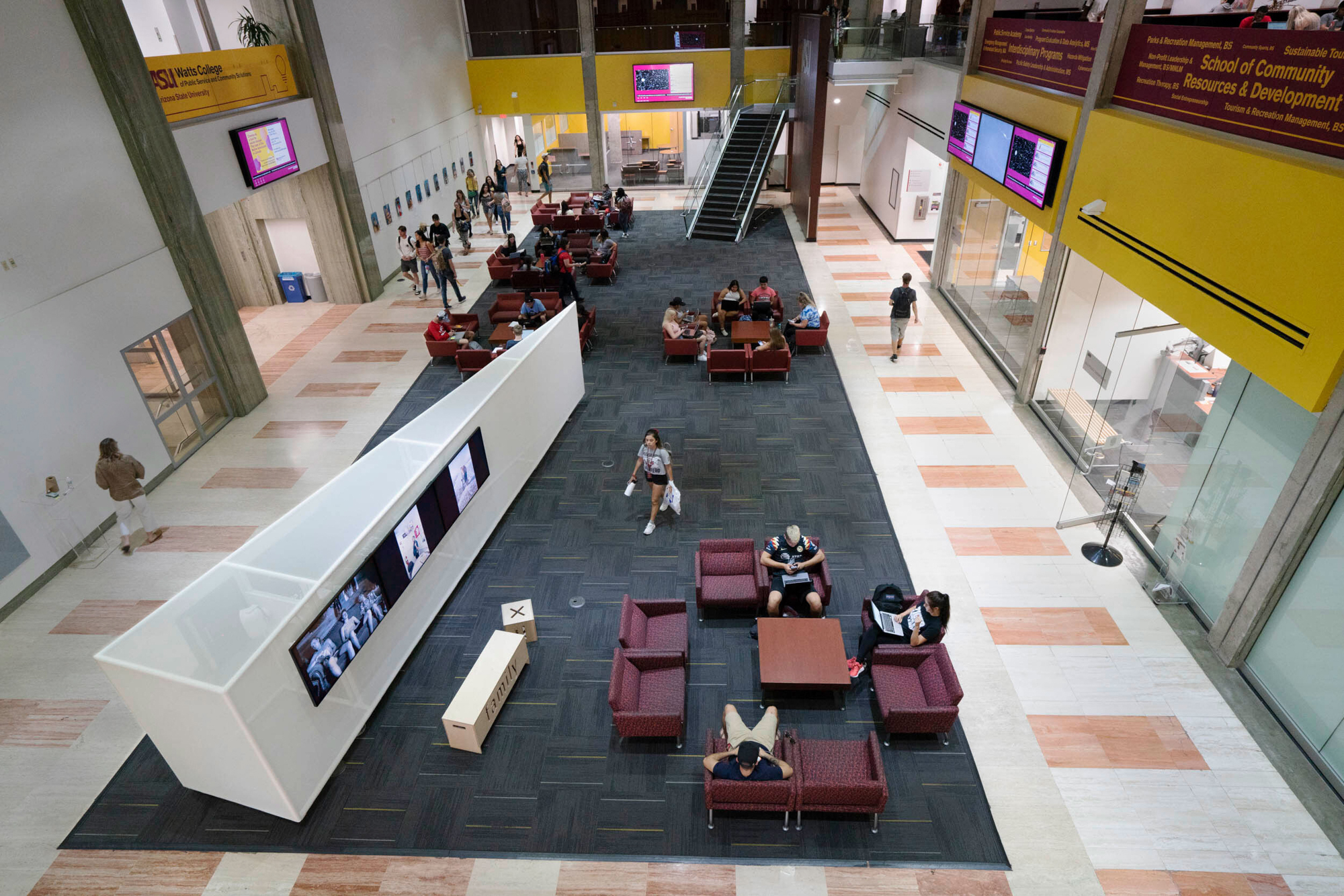 a birds eye view of a common area at Arizona State University with wedge-shaped exhibition panels next to maroon lounge chairs