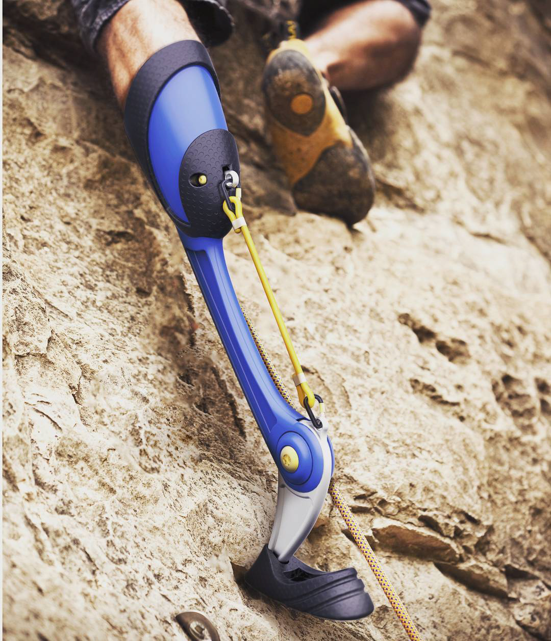 a photograph of a rock climber focused on their prosthetic leg, which is blue, black, and sliver and resembles the leg of a goat