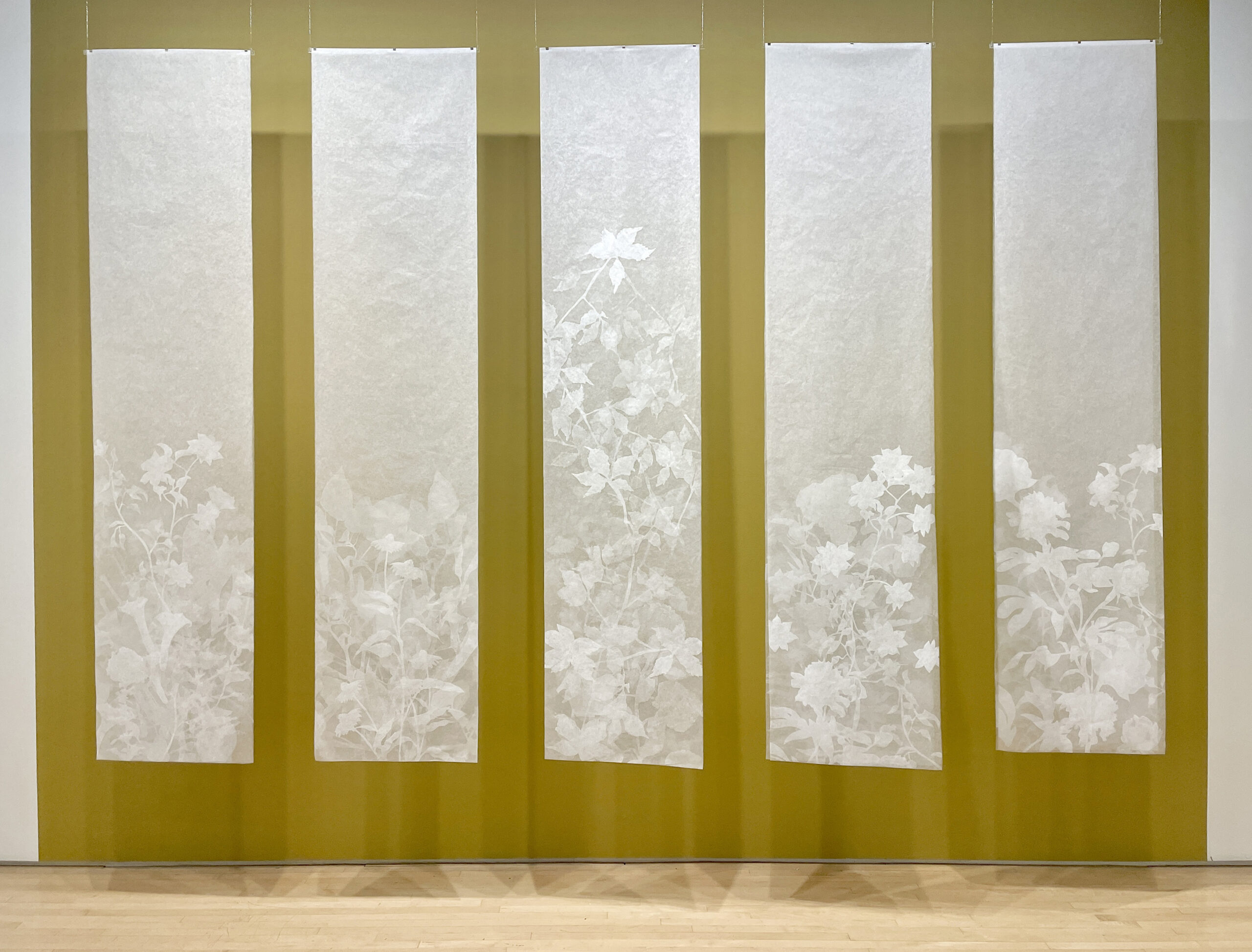 Five off-white columns hanging in a gallery, depicting white flowers.