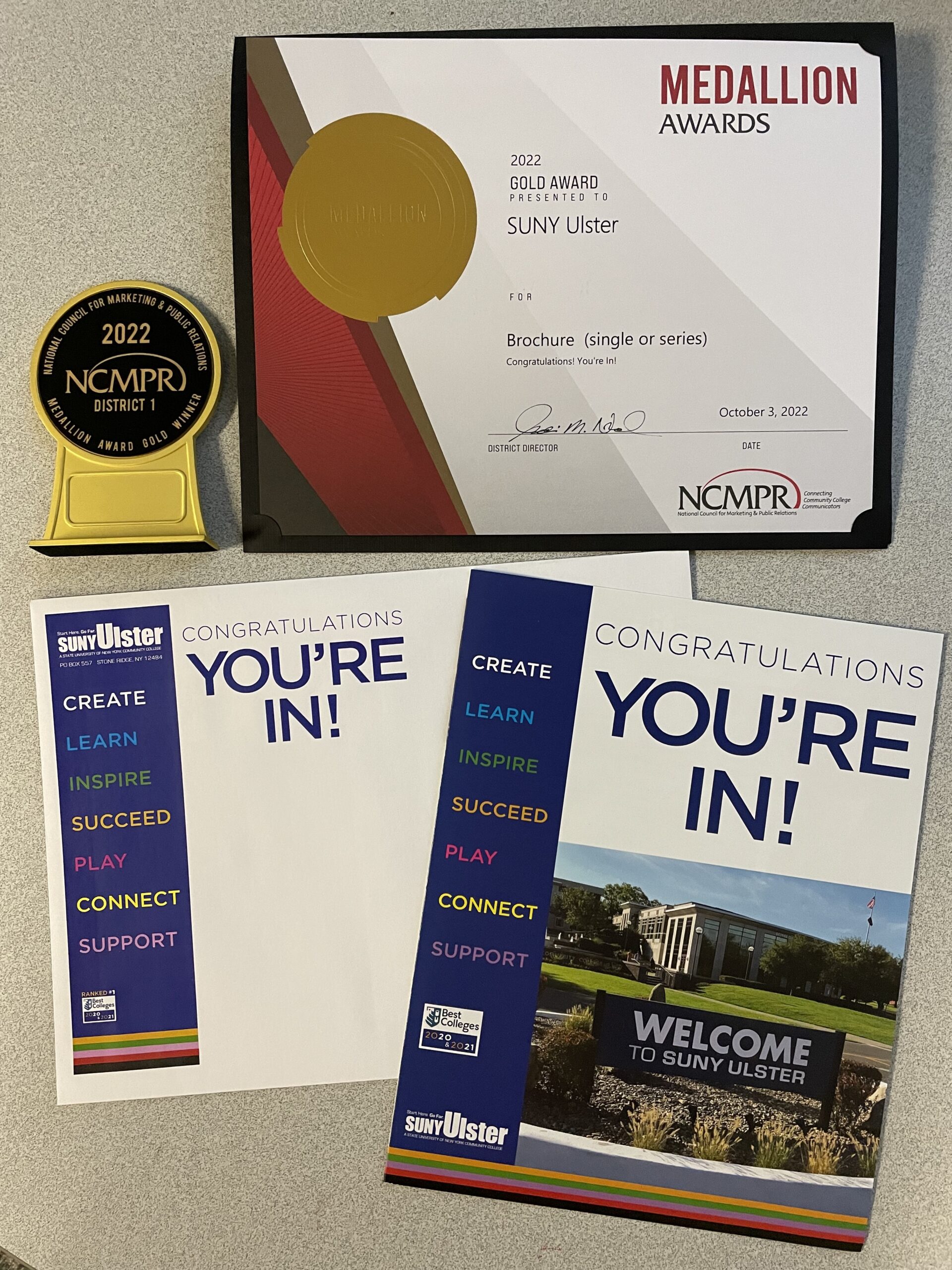 And award certificate, a medallion, and two different papers with the text "CONGRATULATIONS, YOU'RE IN" prominently featured.