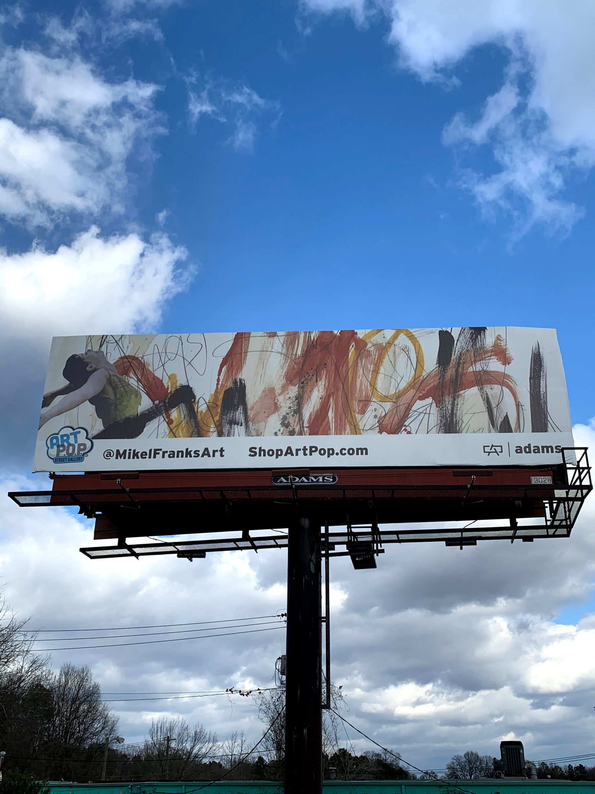 A billboard on a clear day advertising an art show, featuring a dancer and an abstract painting.