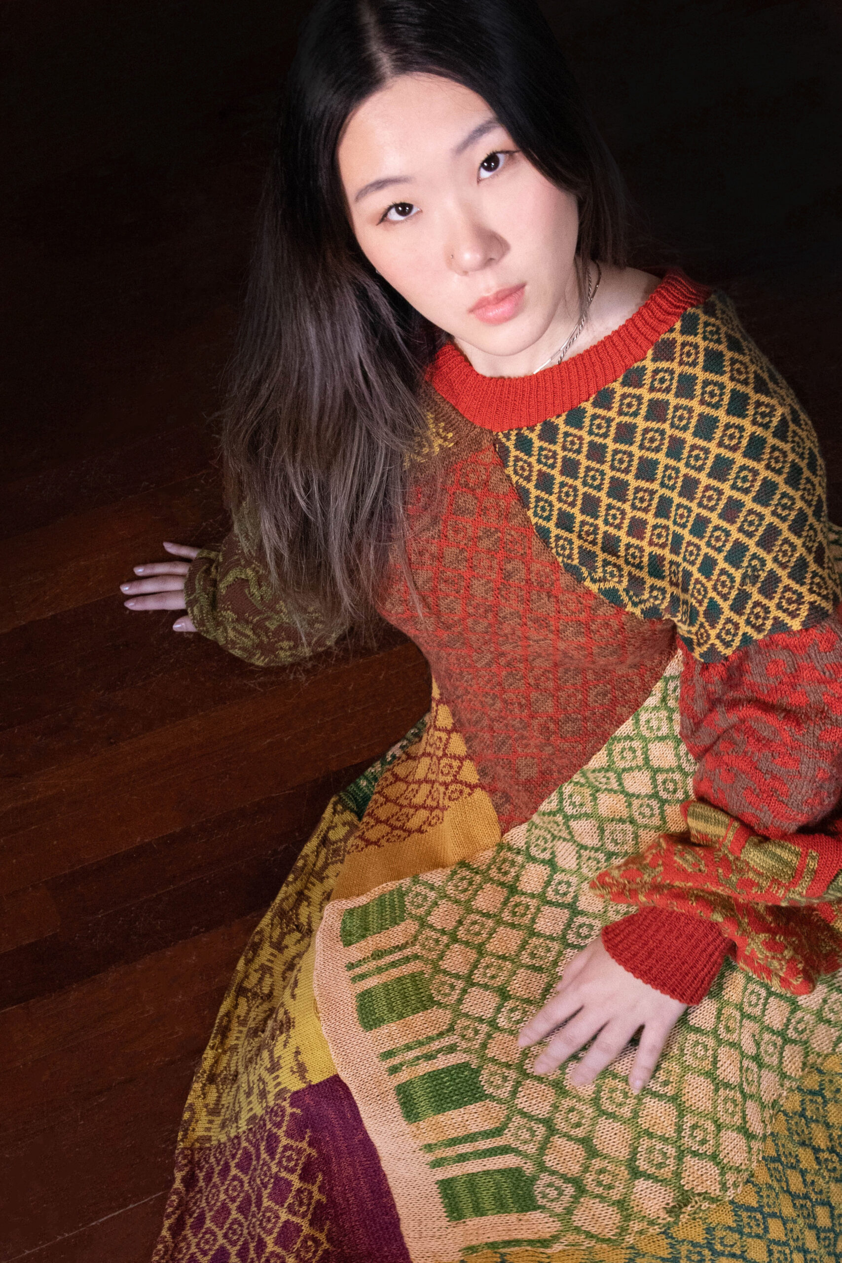 Wearing a knit dress made of rectangular panels, each featuring a different graphic motif, a model poses to show the garment's drape and texture.