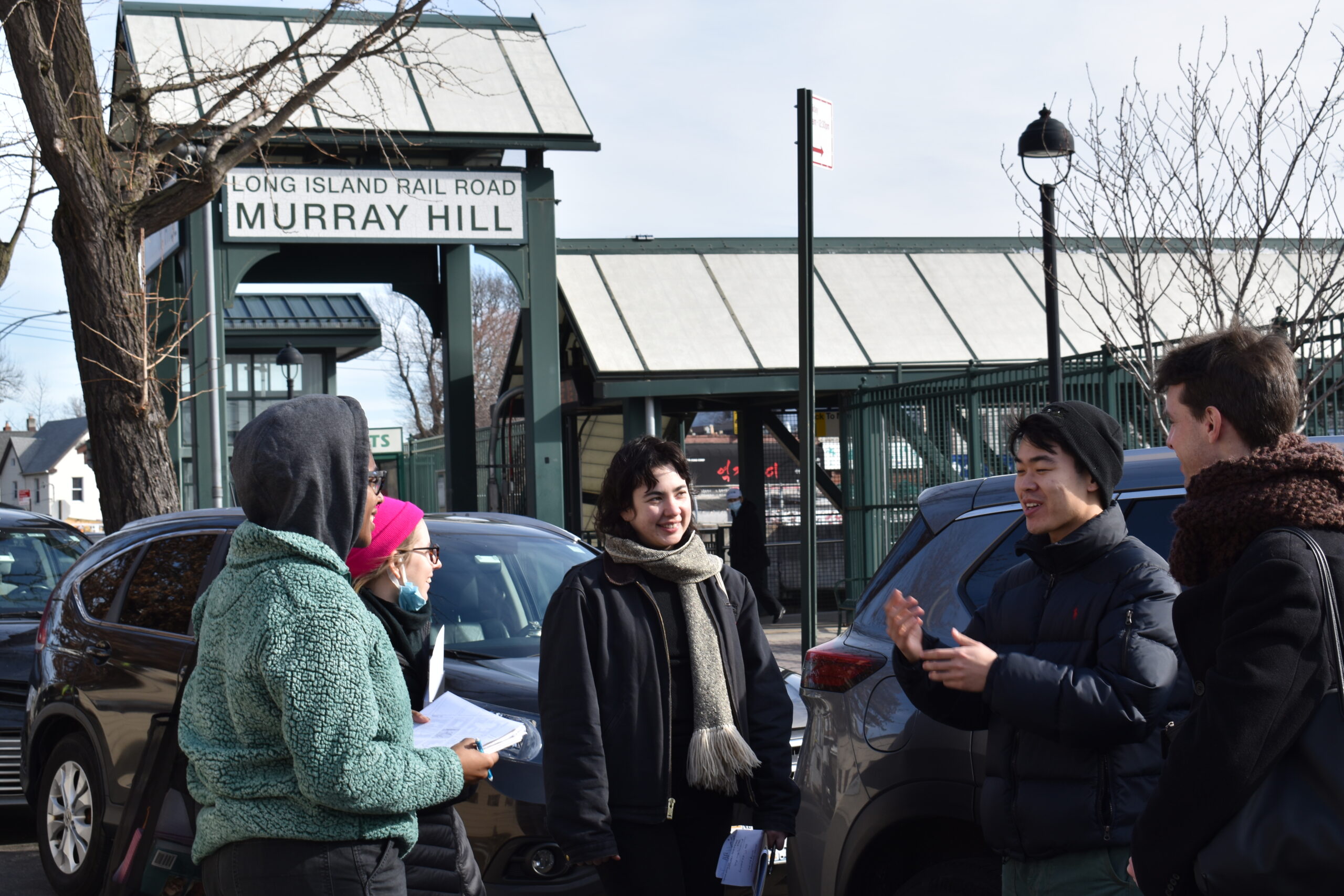 GCPE students, standing in a parking lot having a dialogue in the foreground, with buildings in the background