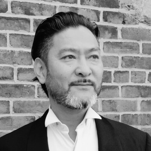Black and white portrait of a man in front of a brick wall.