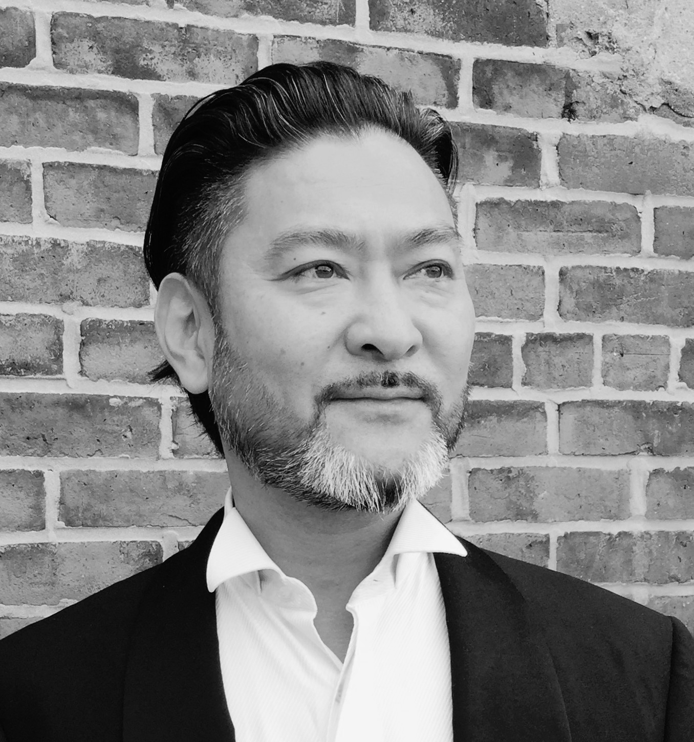 Black and white portrait of a man in front of a brick wall.