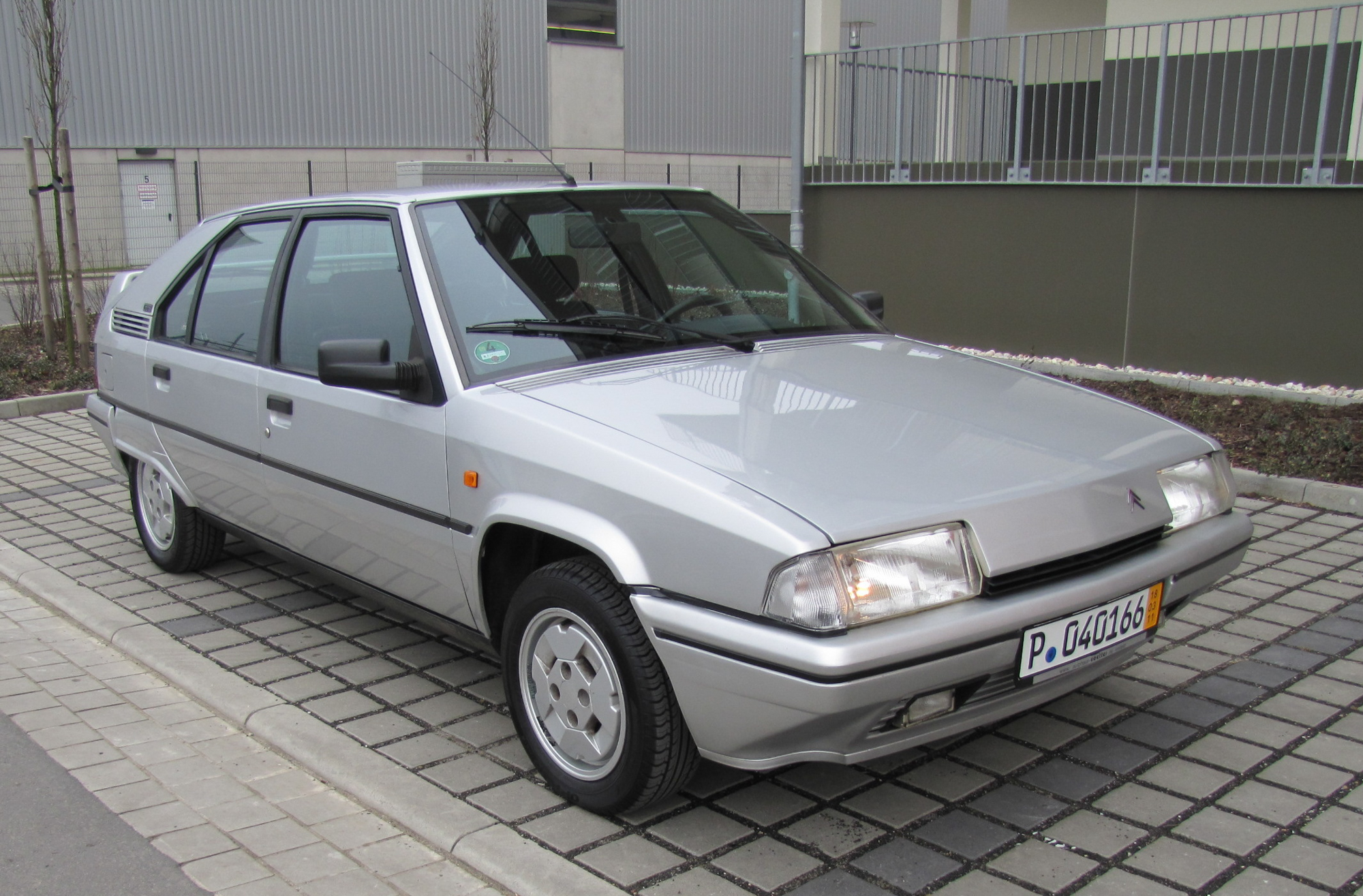 an angular gray sedan parked on a cobblestone driveway