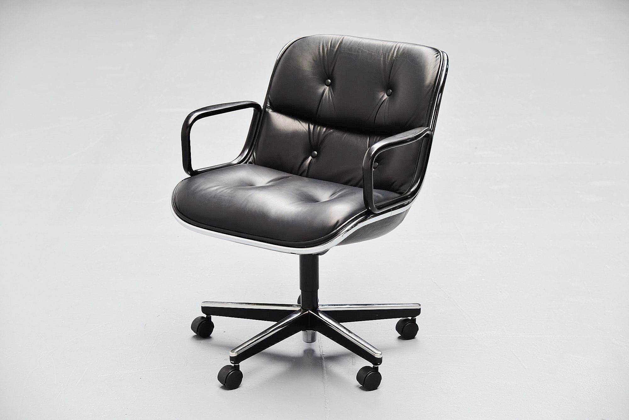 a black leather upholstered chair with armrests and five wheels on its base