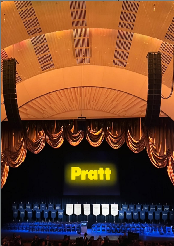 A photograph from the seats in Radio City Music Hall showing the stage before anyone was one it. There is a large yellow Pratt above where everyone will be sitting.