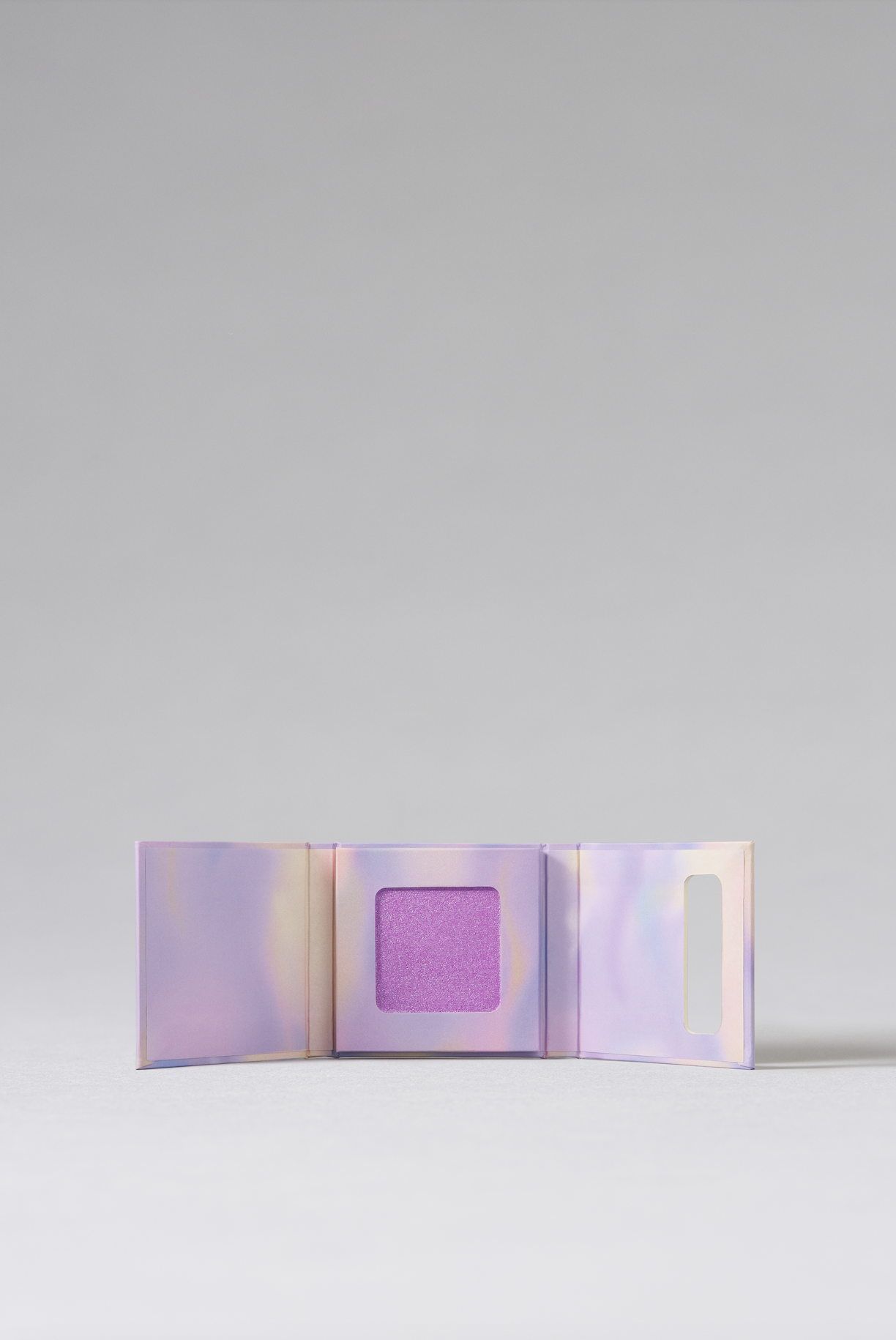 The three-part interior of a makeup box which is colored mesh purple and with a glittery square of purple makeup contained in the center third.