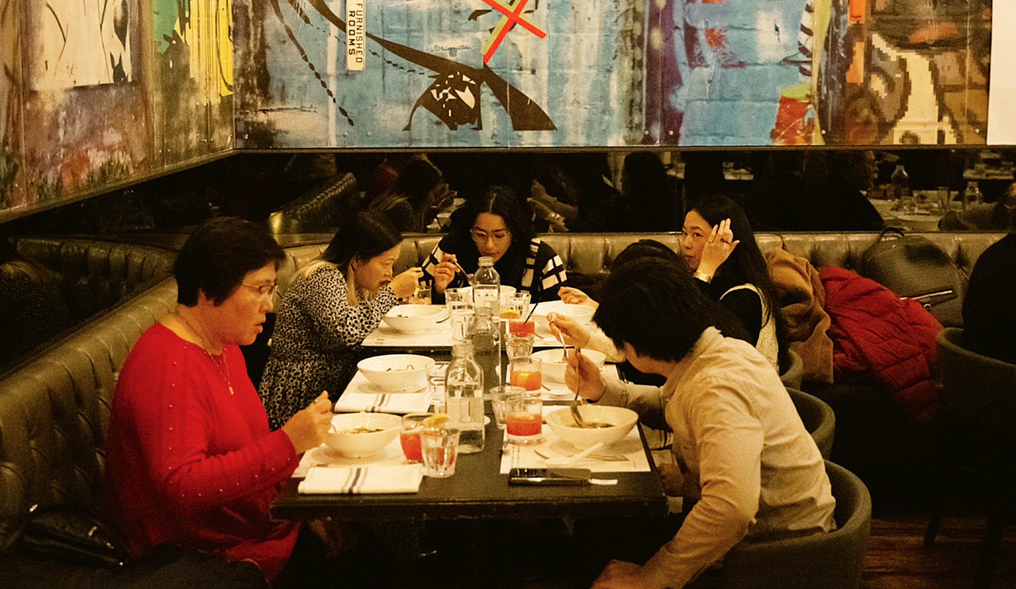 A group of diners eating soup from large ceramic bowls around a cushioned banquette