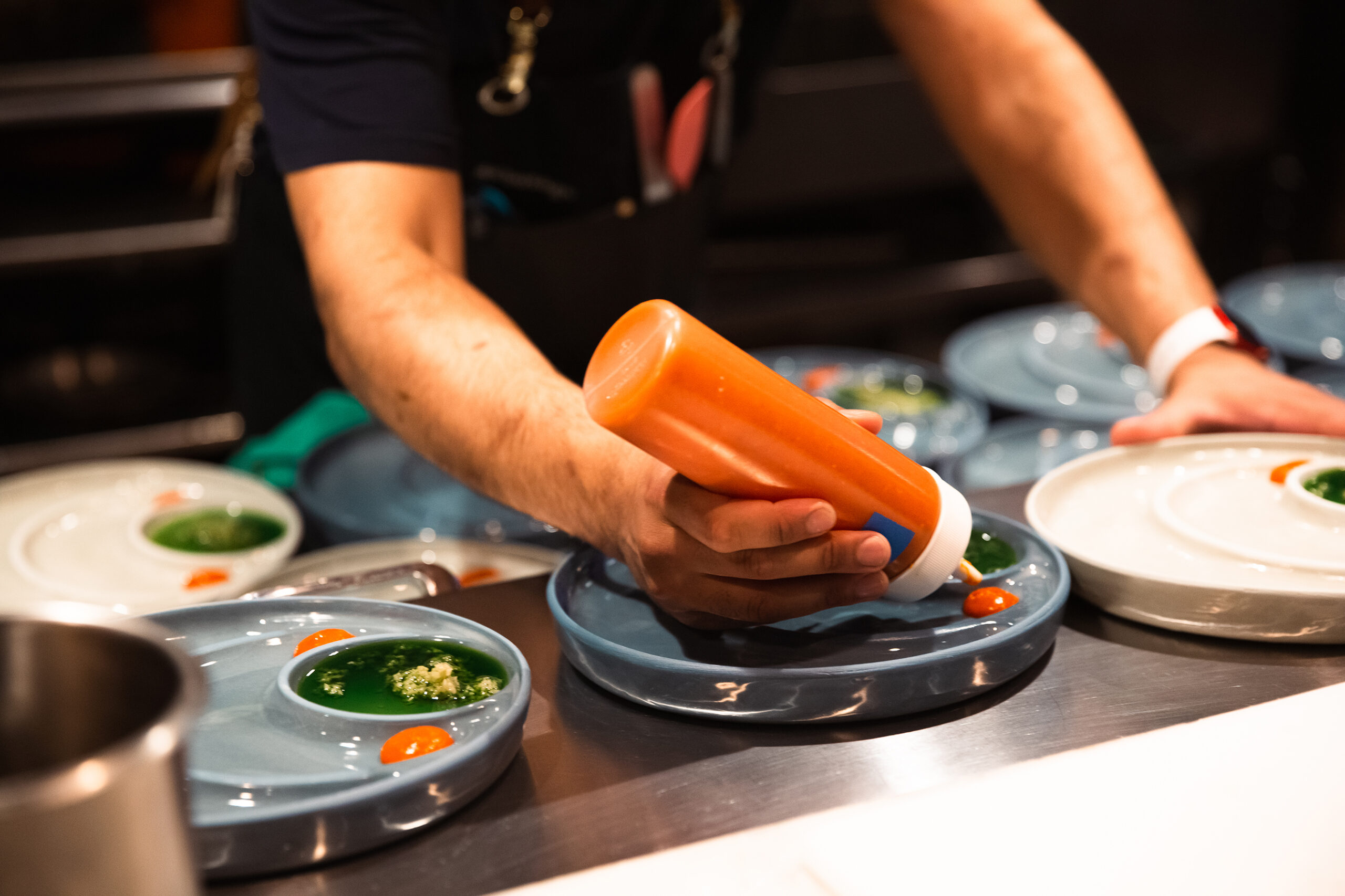 Close-up of segmented bowl plate as a chef dresses it with dollops of orange-red sauce