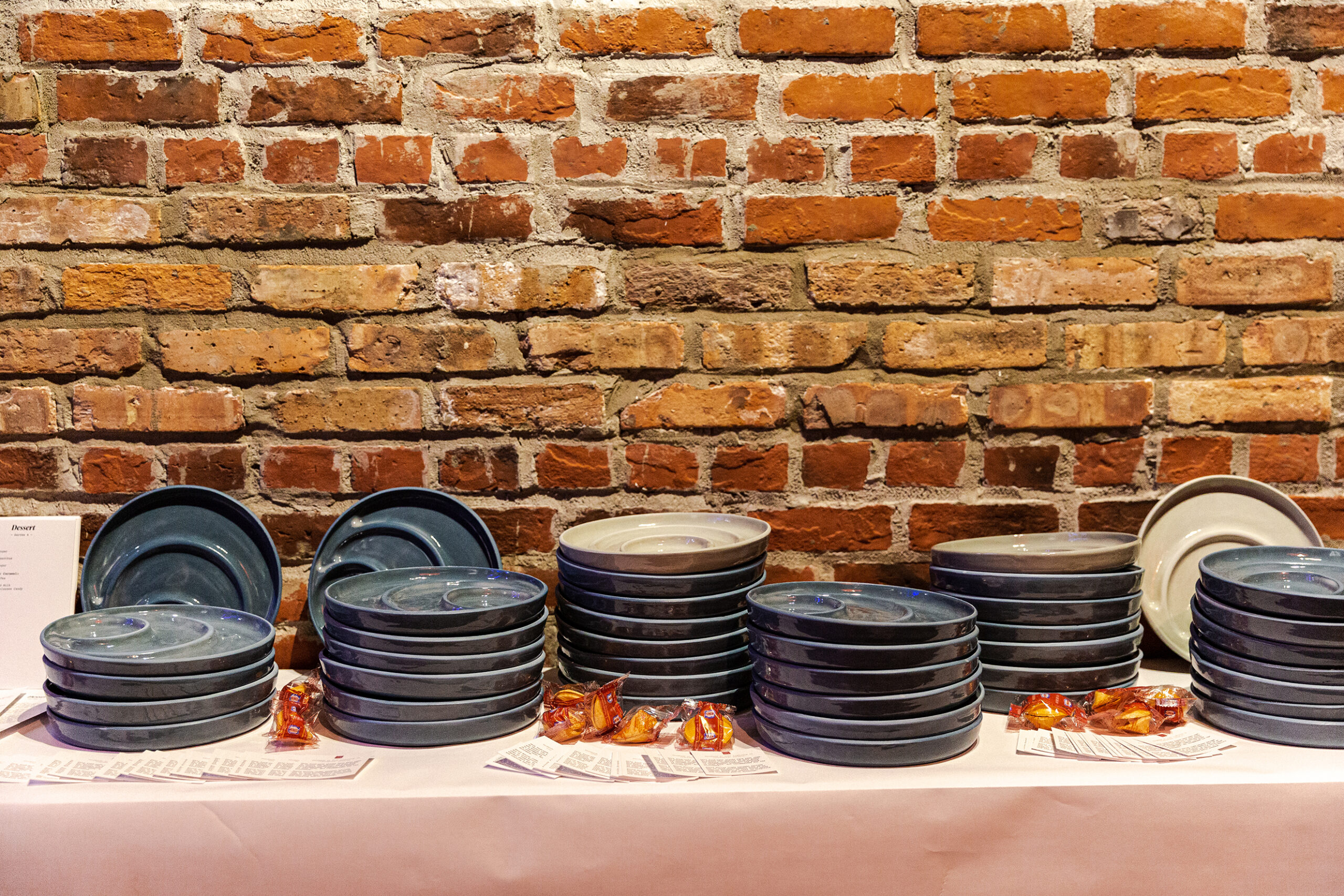 Stacks of gray bowl-plates on a table in front of an exposed-brick wall