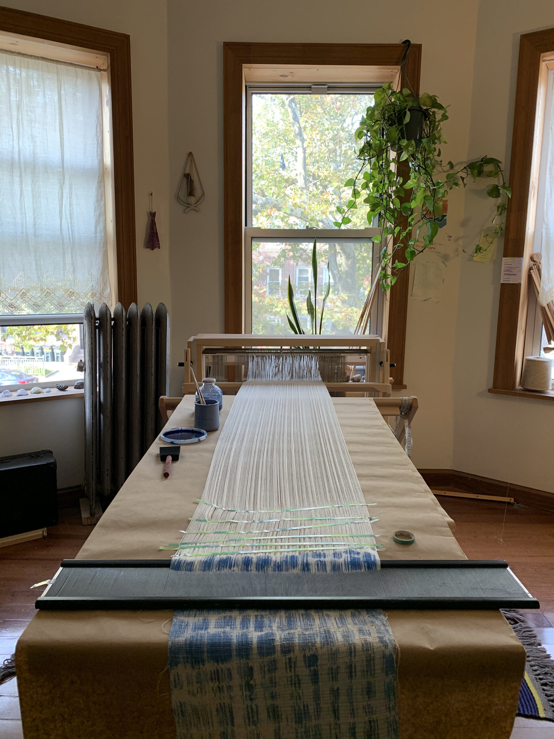 Weaving in progress on a long table in a studio alcove with three windows