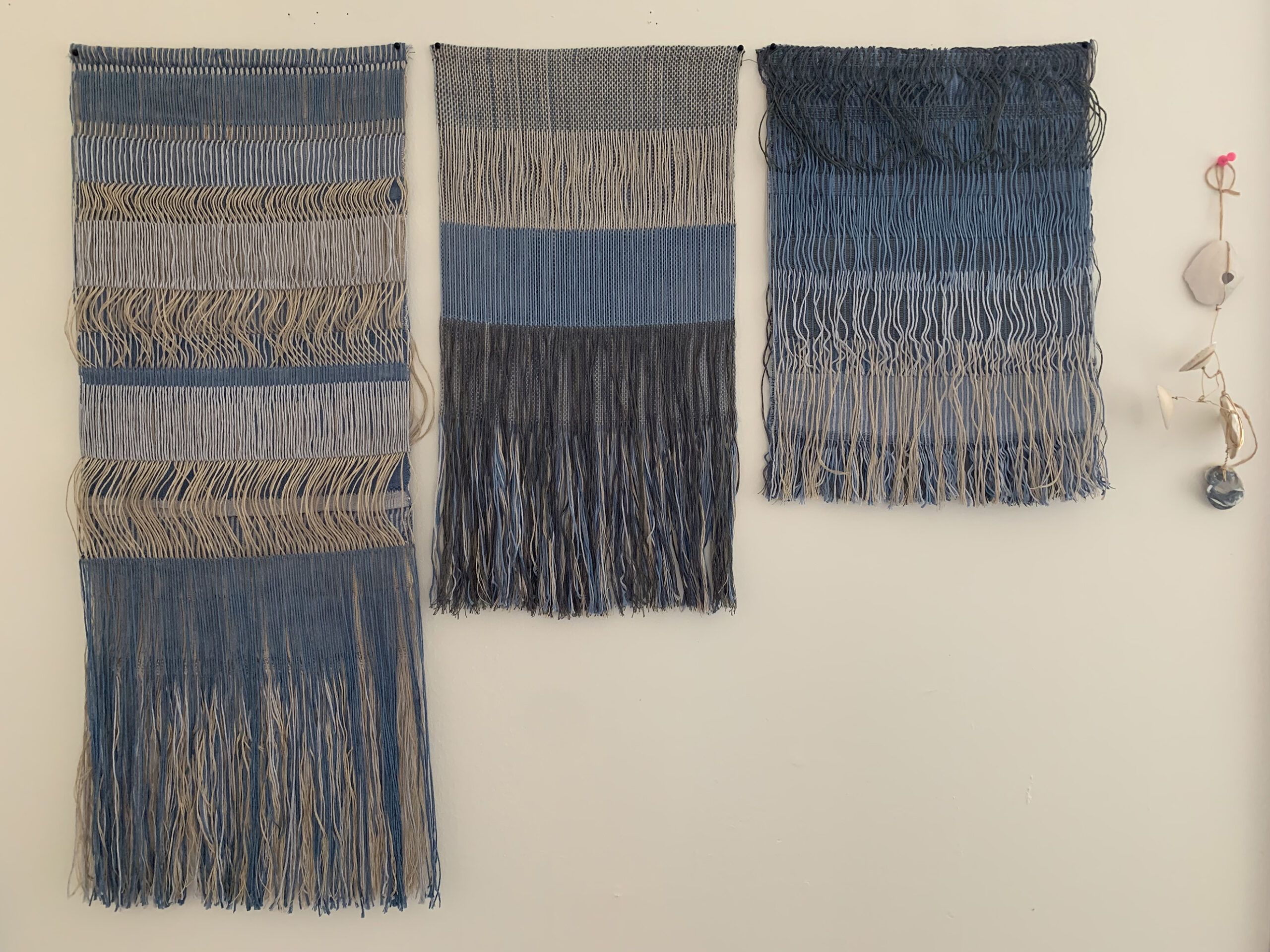 Three hanging woven tapestries made with shades of blue, gray, and white fibers