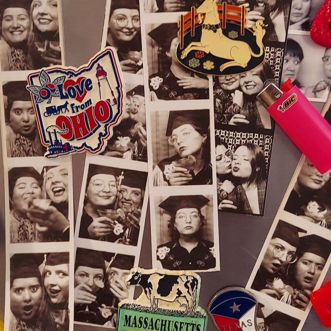 A closeup photo of a refrigerator door covered in photo booth prints showing different confirgurations of one or two students dressed in their caps and gowns. The photo strips are being held up by magnets.