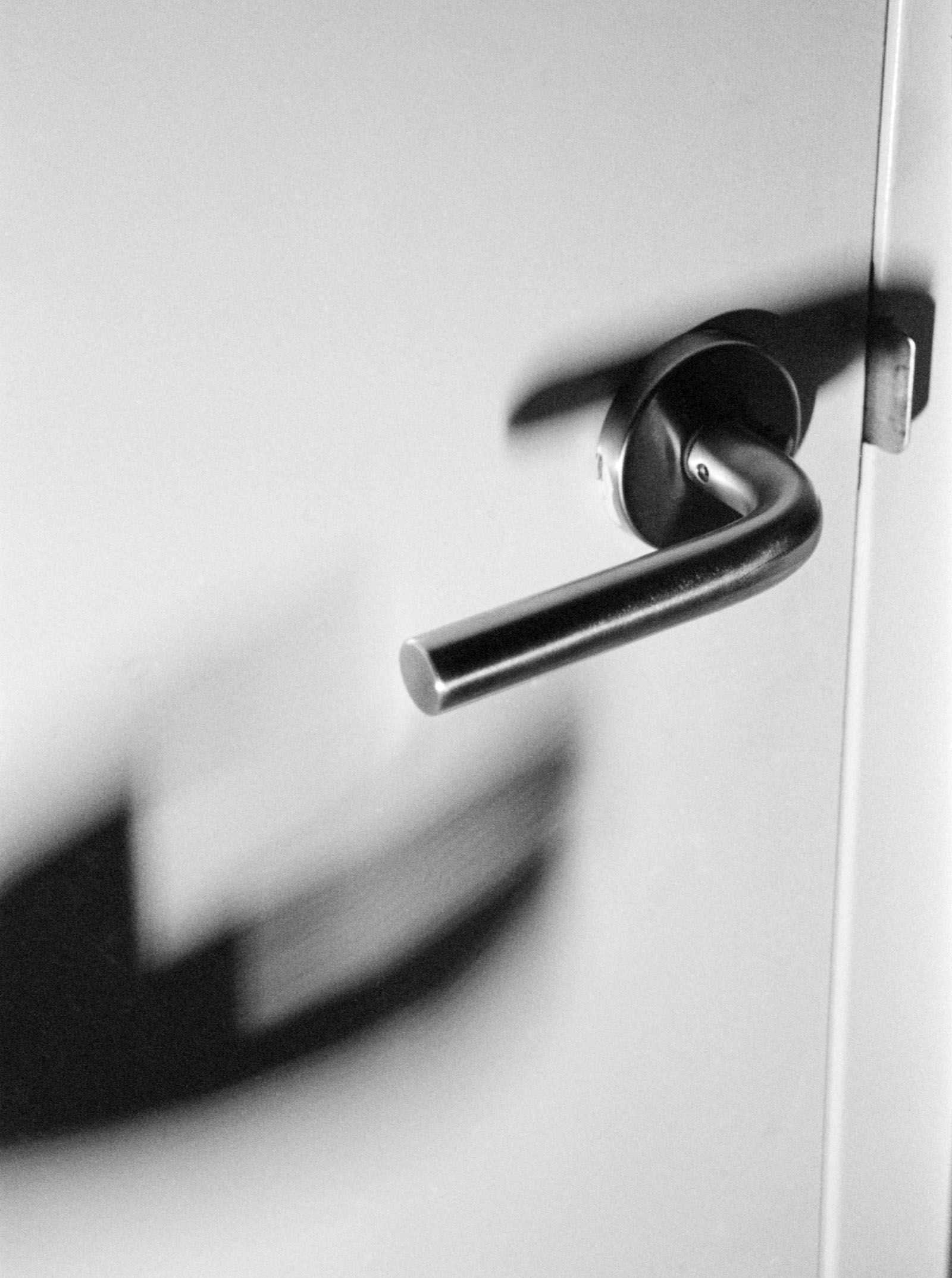 A black and white photograph of a closed door focusing on the handle.