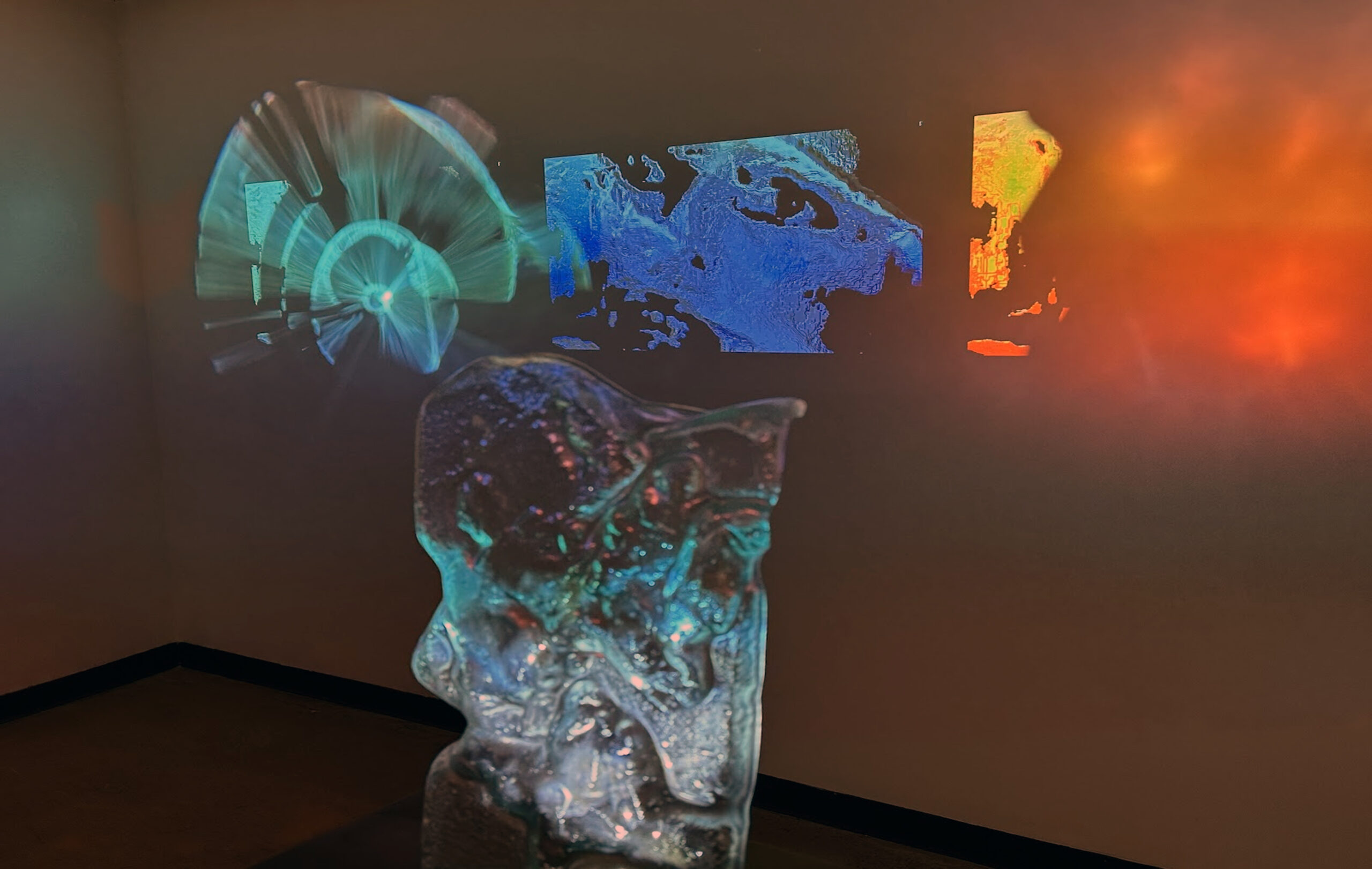 projection of womans face, with post-processing added on wall, behind a clear sculpture, closer vantage